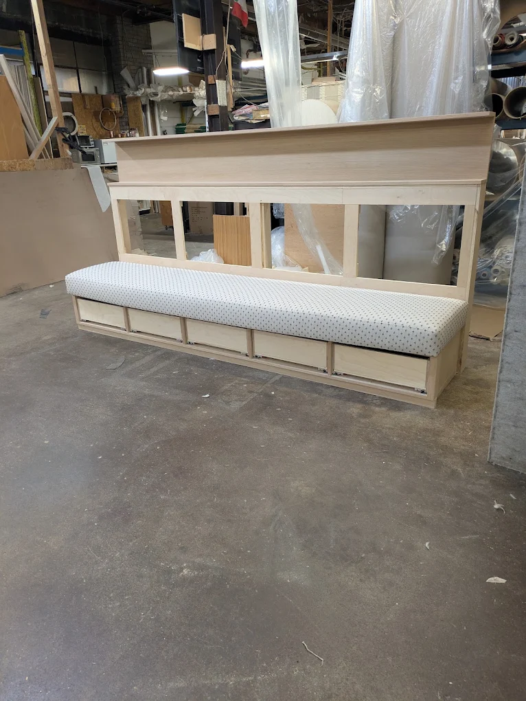 Unfinished maple banquette with an upholstered seat and five storage drawers, in the workshop